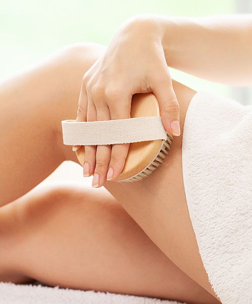 drentox-Cellulite treatment, woman arm holding dry brush to top of her leg.